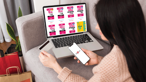 A woman using a laptop displaying shopping items and a smartphone with a credit card in hand.